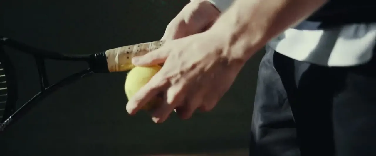 Close-up of a hand bouncing a tennis ball before serving, dramatic side lighting