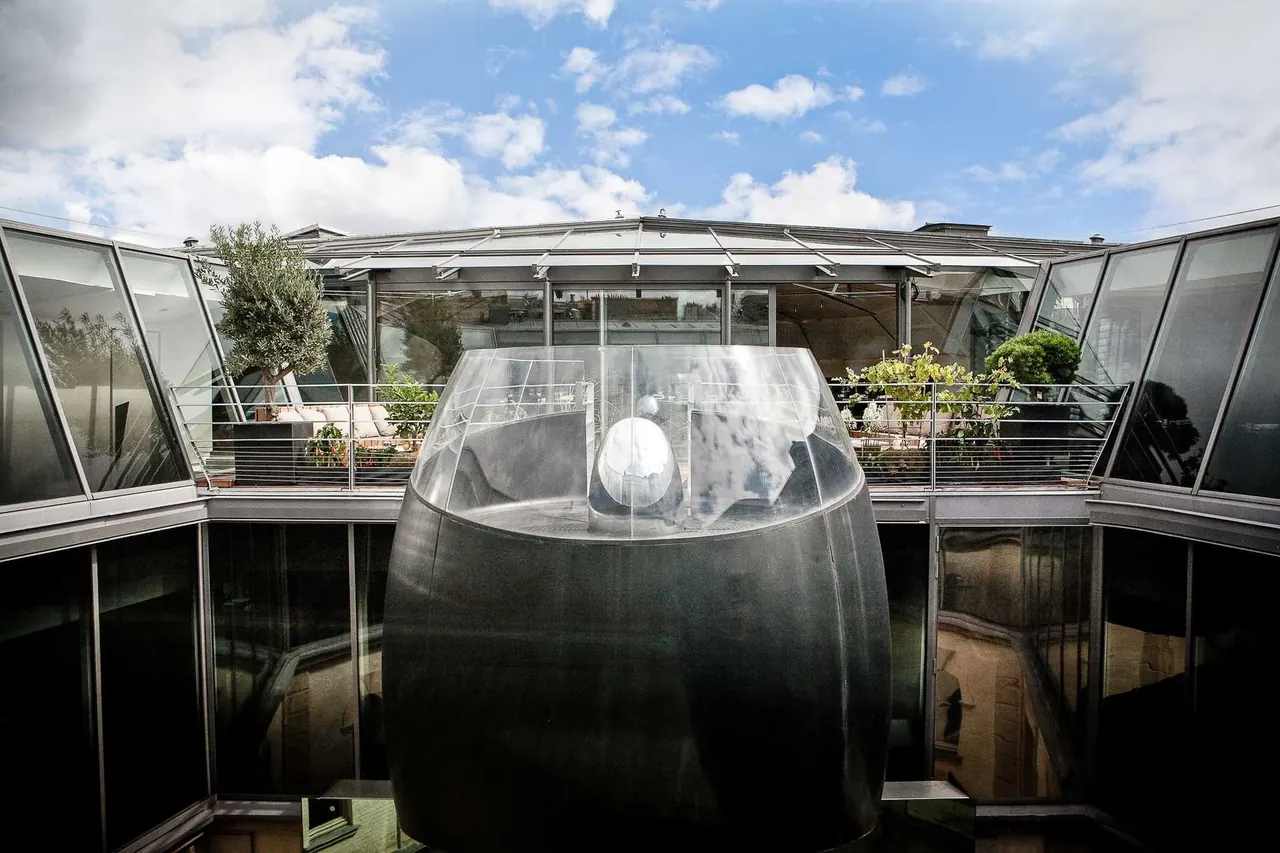 Glass-roofed Paris rooftop terrace with a sculptural centerpiece and olive trees