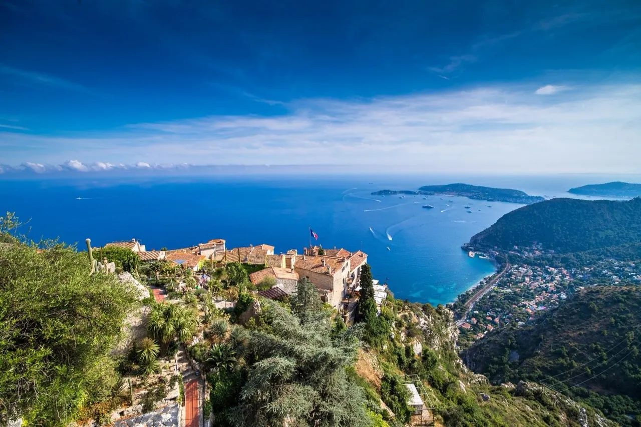 Aerial view of a clifftop medieval village overlooking a deep blue Mediterranean bay