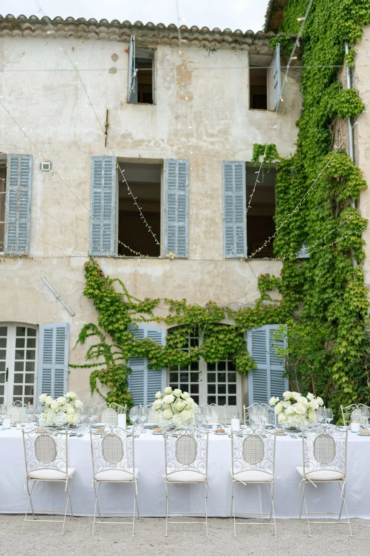 Long table dressed with white roses in front of an ivy-clad stone farmhouse