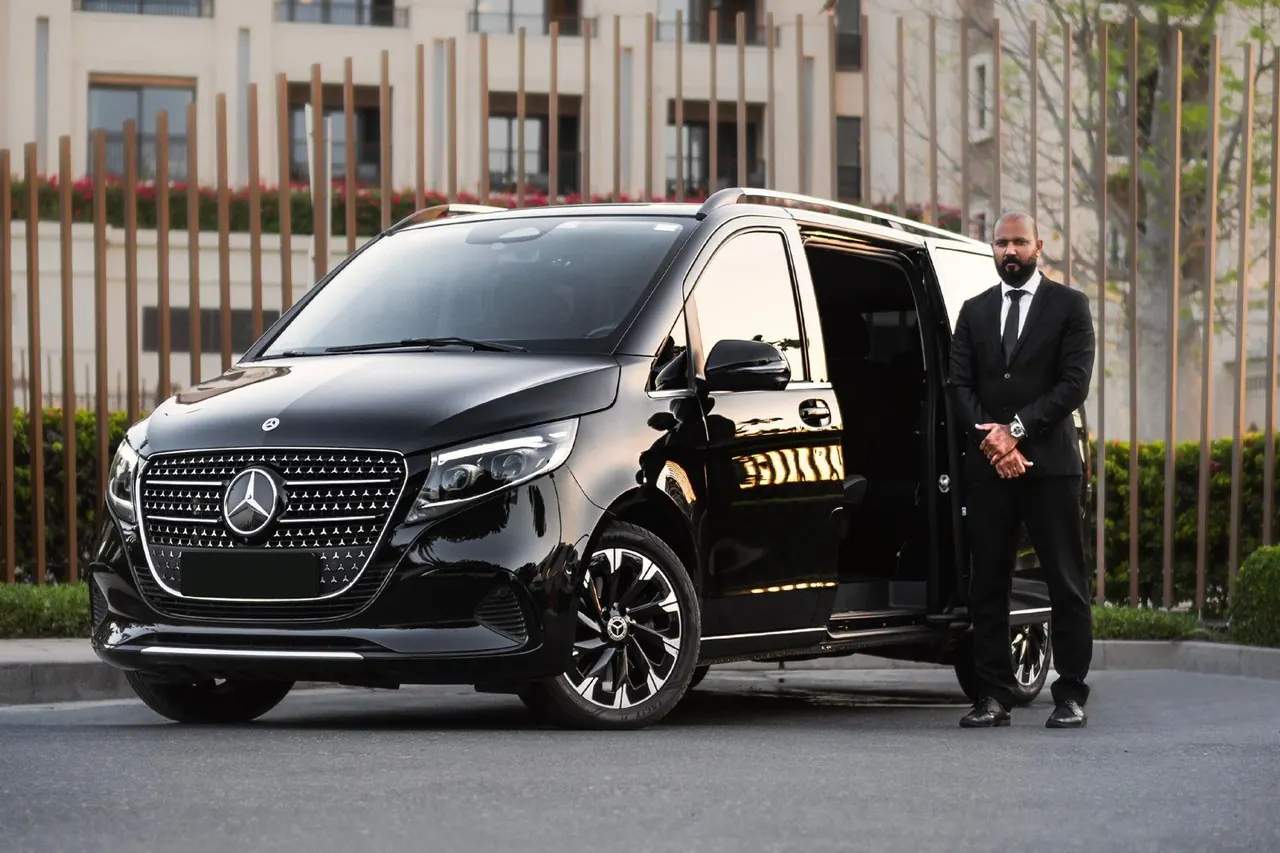 Chauffeur standing beside a black luxury van with the door open for a VIP transfer